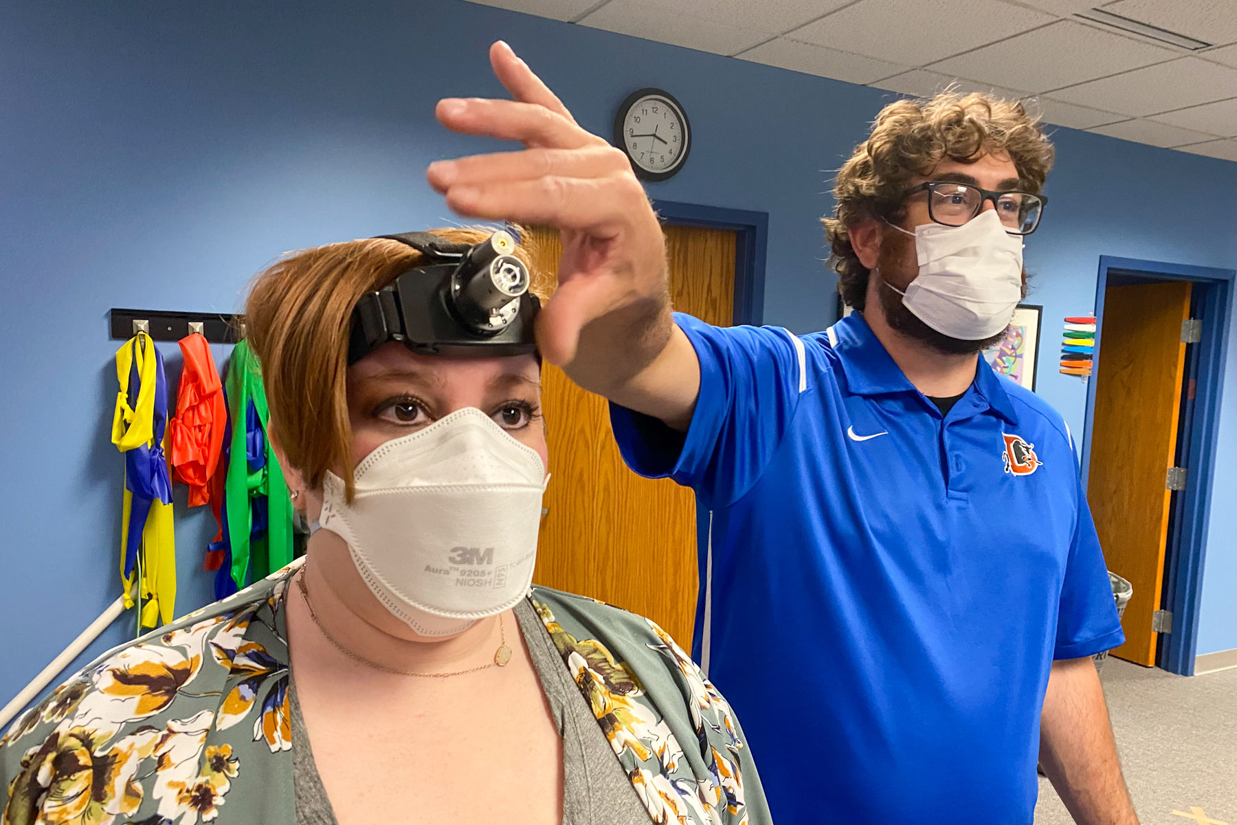Long COVID patient Alex Trebino and physical therapist Dan Stoot at High Definition Physical Therapy in Englewood. Some of her therapy involves tracing images on a wall using a laser on a headlamp and others in her hands.