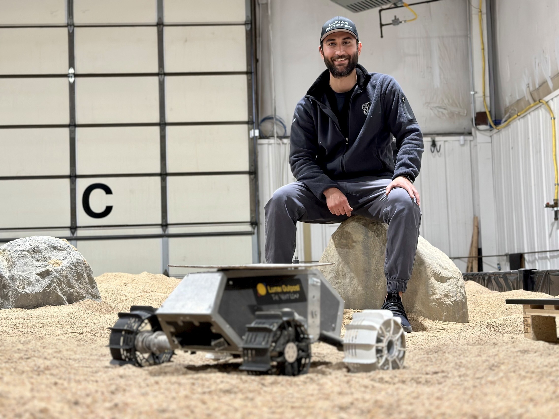 Justin Cyrus poses with a small test rover at Crater Beach in a warehouse in Arvada that simulates conditions on the moon.